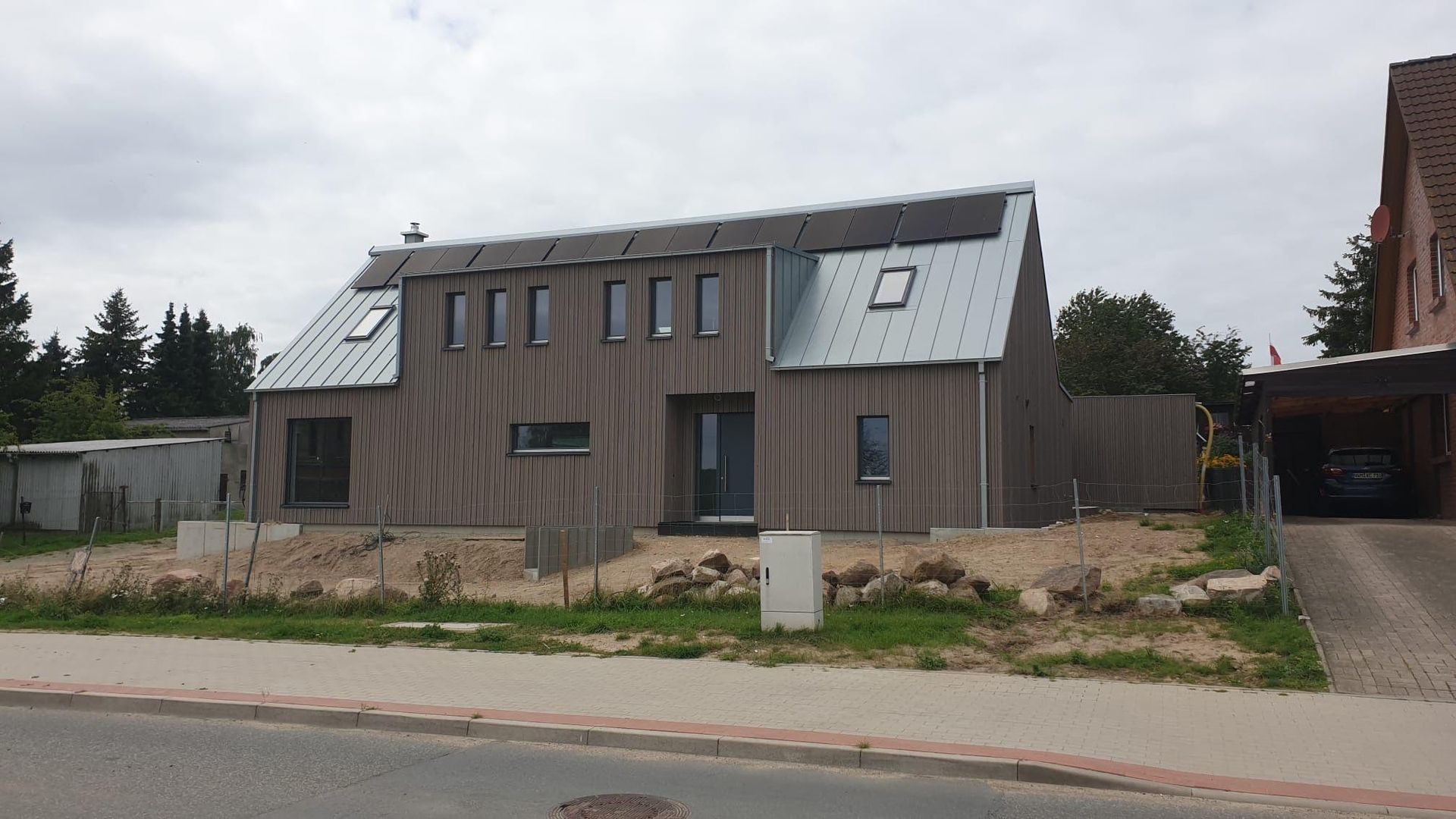 Außenansicht eines Neubaus mit grauer Holzfassade und Dachfenstern von der Straßenseite aus