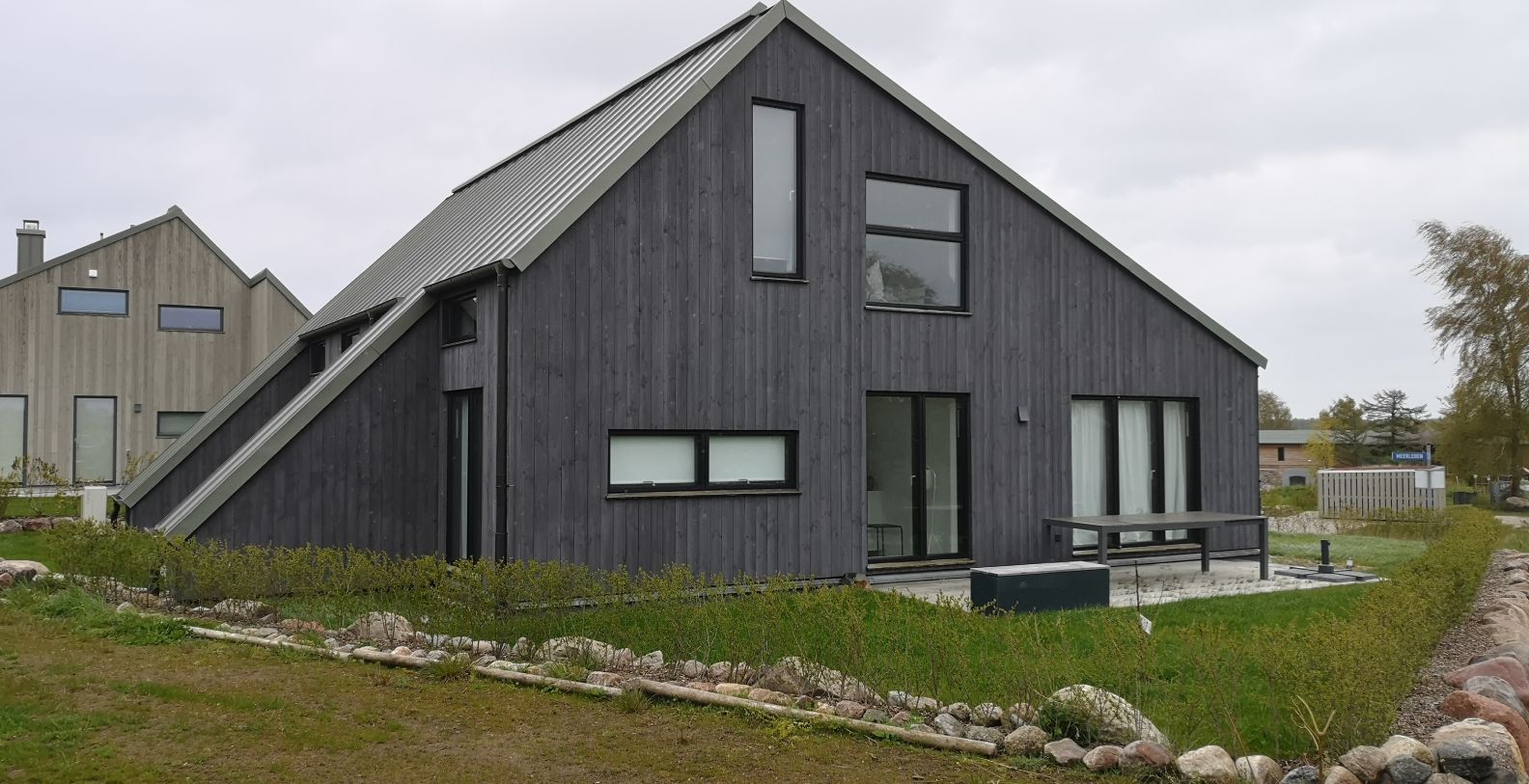 Modernes Wohnhaus mit dunkelgrauer Holzverkleidung asymmetrischer Architektur und Steingarten-Einfassung